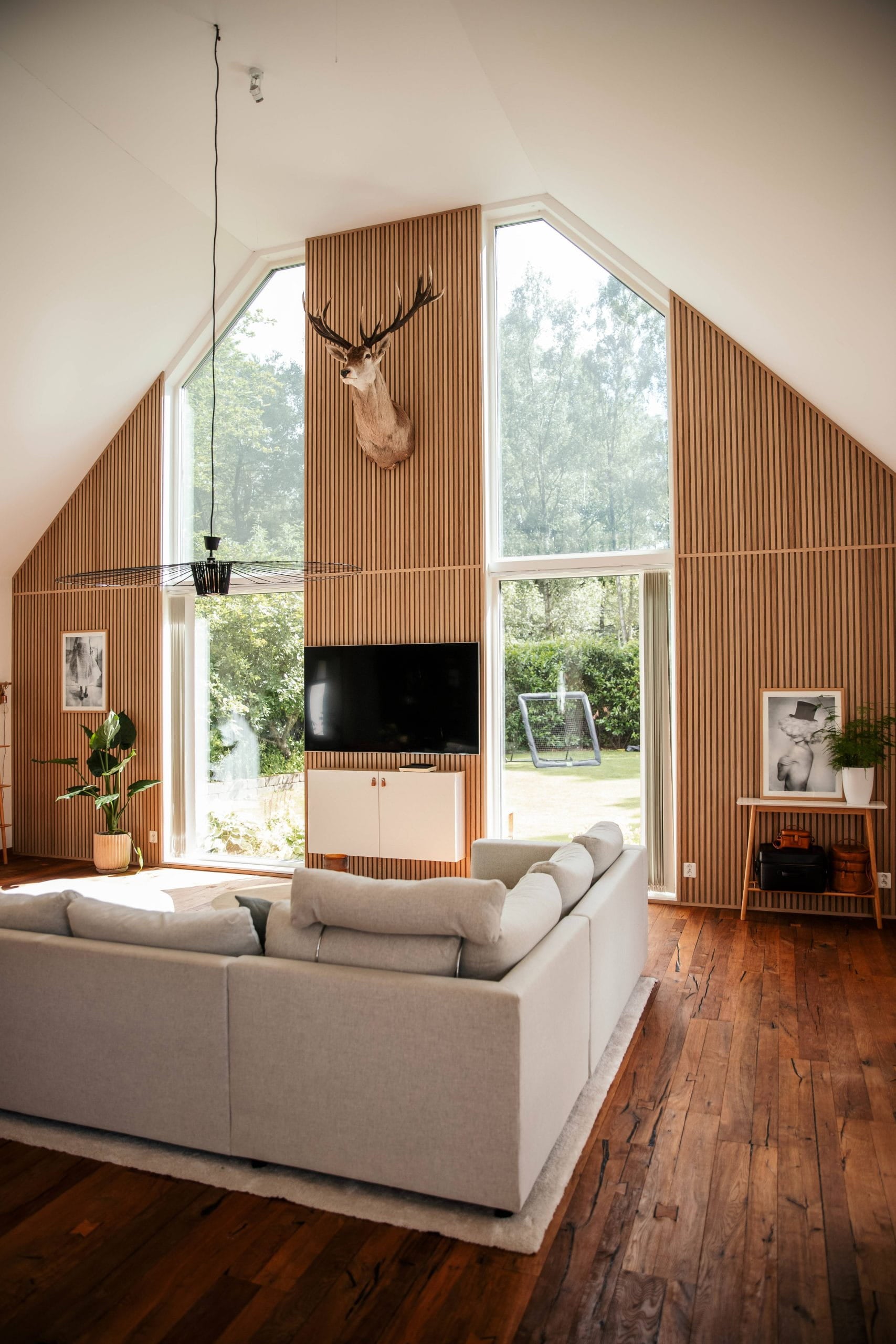 Akupanel acoustic wood slat wall panels on a vaulted interior wall with tall windows and a sofa.